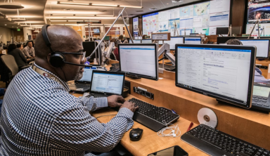 IT management control room with technician monitoring multiple computer screens.